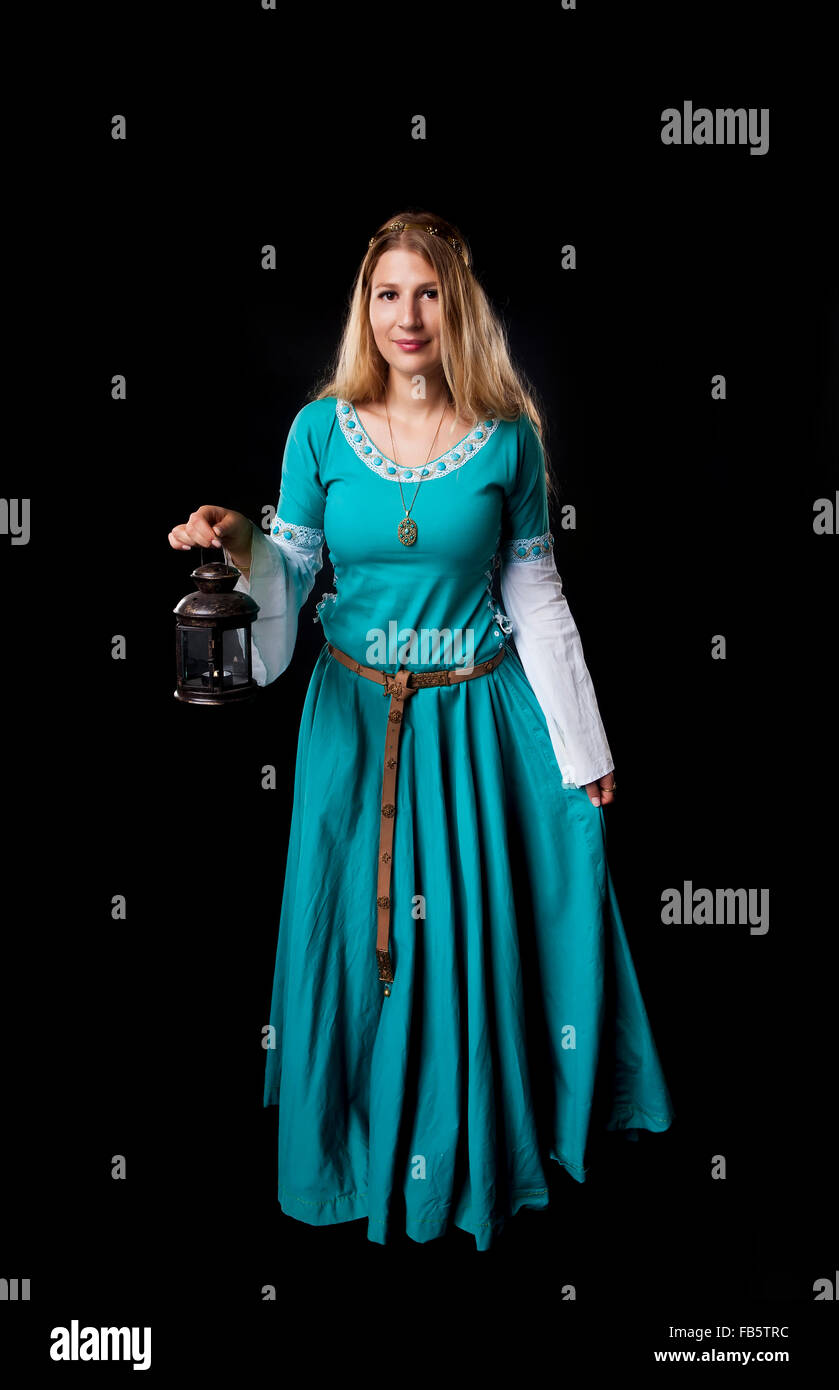 Studio shot of beautiful girl dressed in a medieval turquoise dress holding a retro style lamp on black background Stock Photo