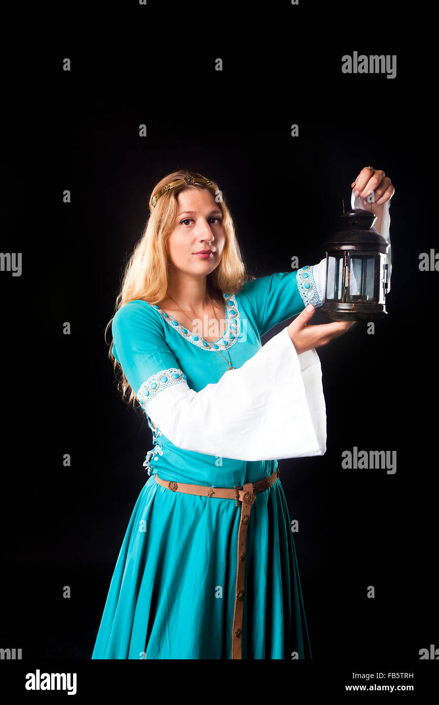 Studio shot of young girl in a medieval turquoise dress looking at the camera while holding up a retro style lamp (portrait on b Stock Photo