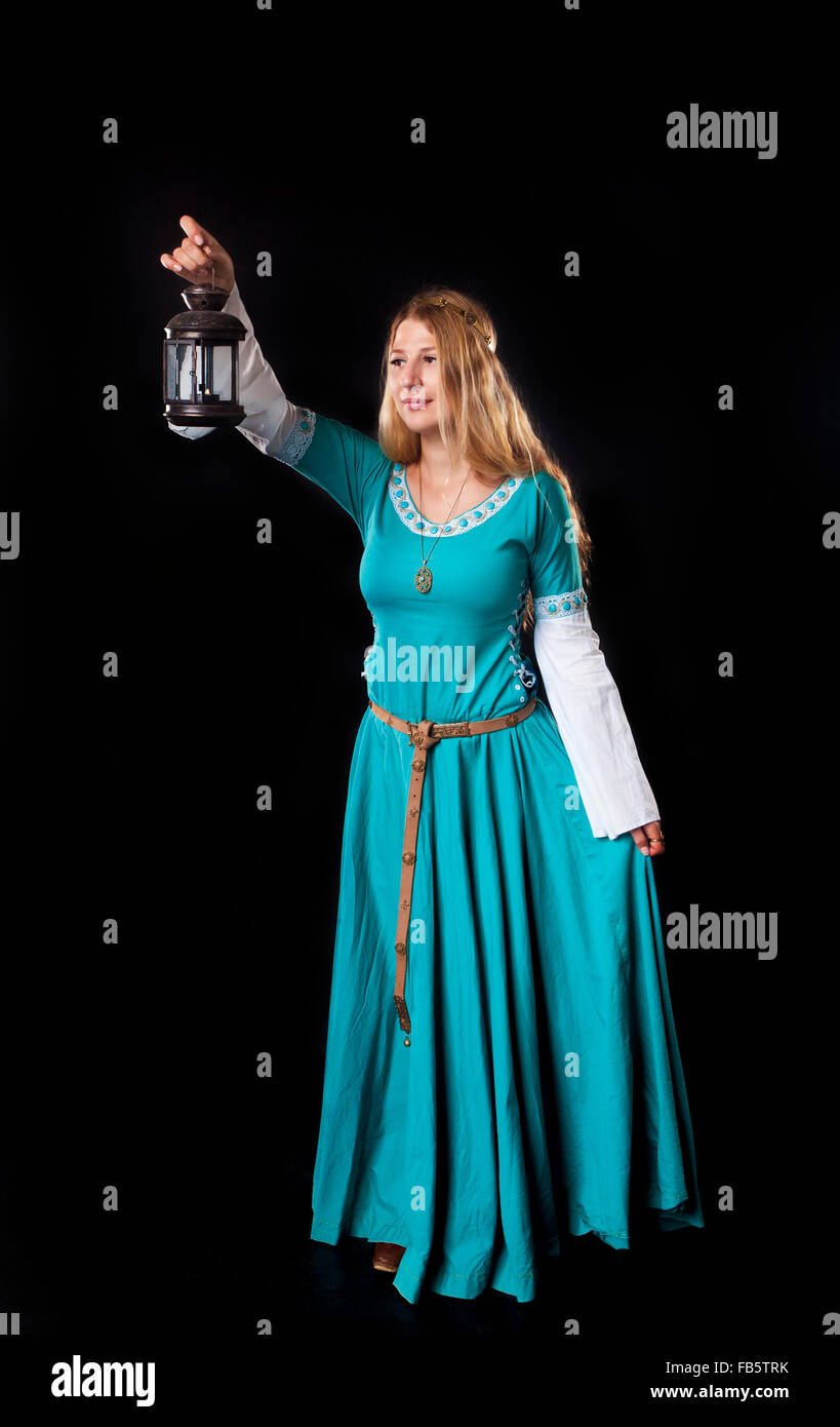 Studio shot of young girl dressed in a medieval turquoise dress holding up a retro style lamp on black background Stock Photo