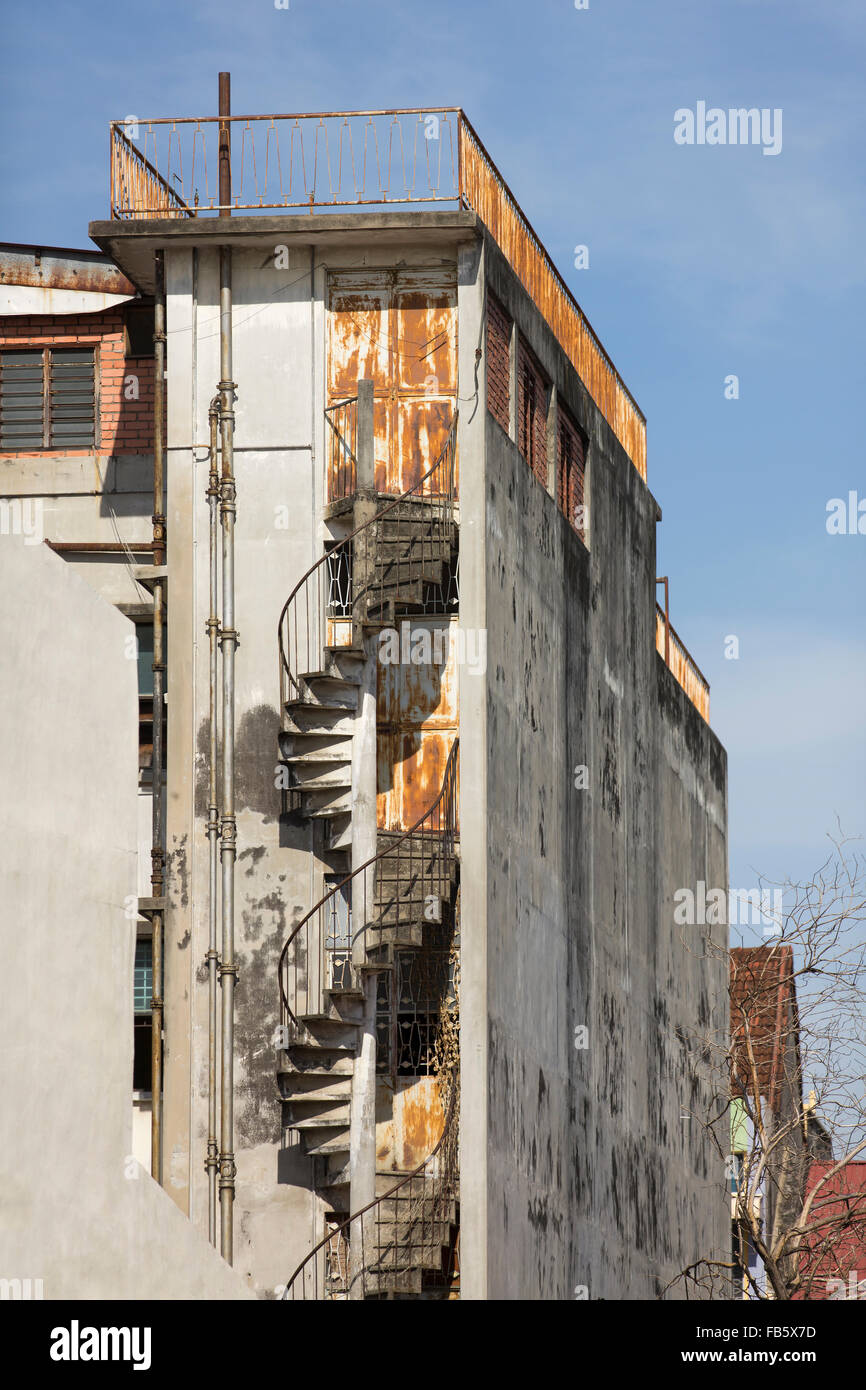Rusting fire escape on a derelict building. Rust and flaking paint on an old apartment block set against a blue sky in Penang. Stock Photo