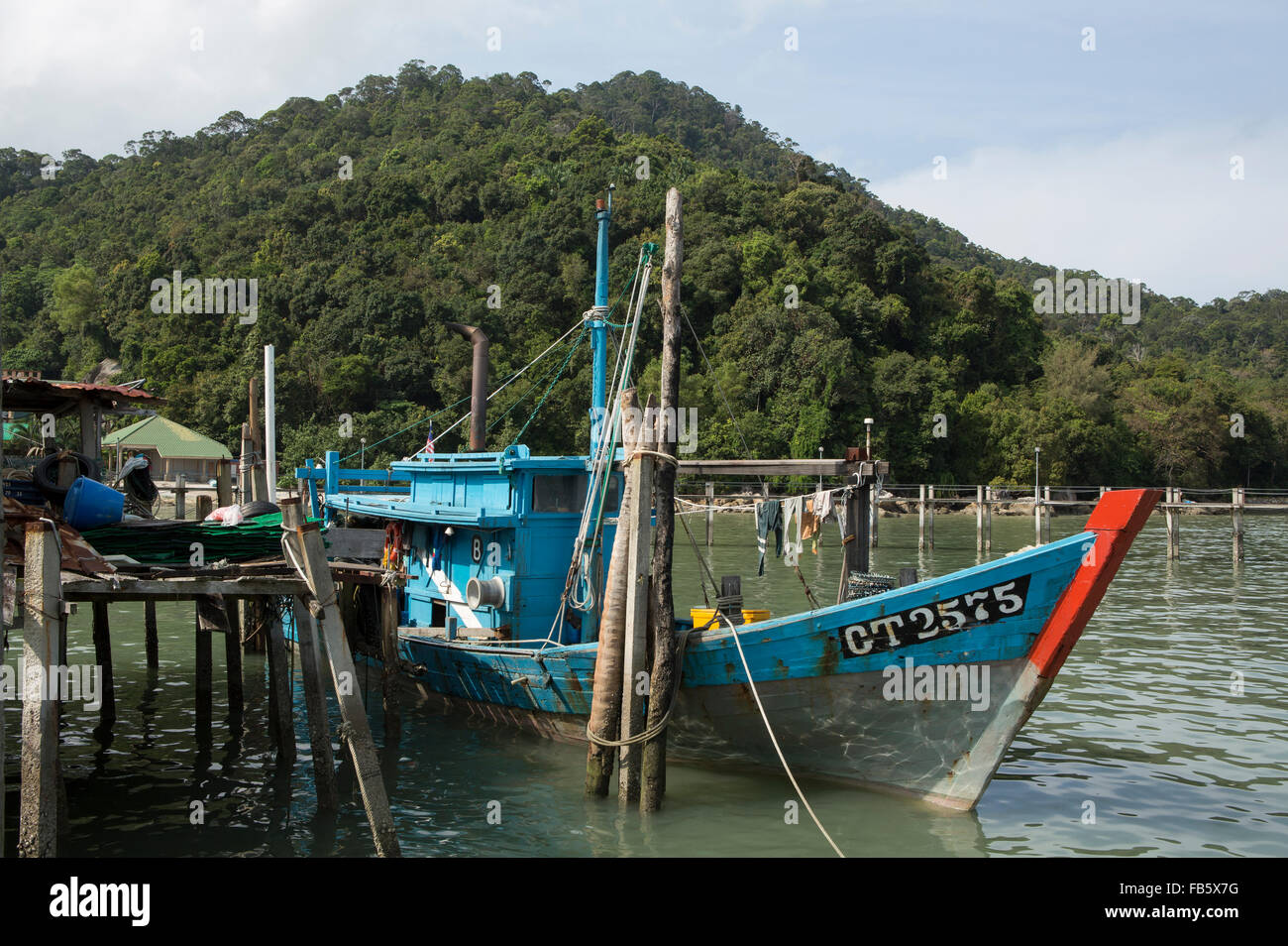 Old fishing boat tied up alongside an old jetty at Teluk Bahang in Penang Malaysia. Green hills of the national park behind. Stock Photo