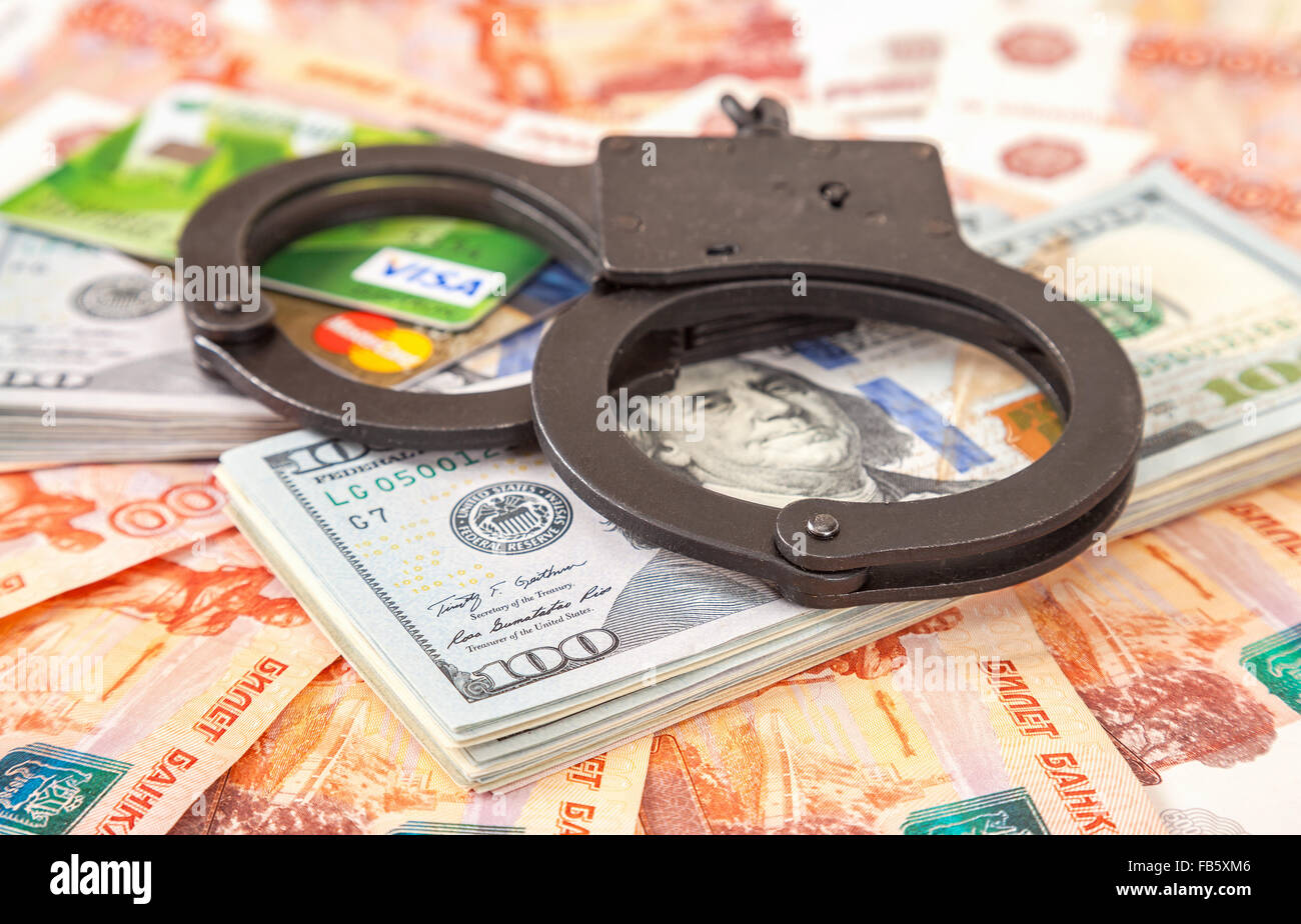 Steel handcuffs lying on a stack of dollar bills and credit cards Stock