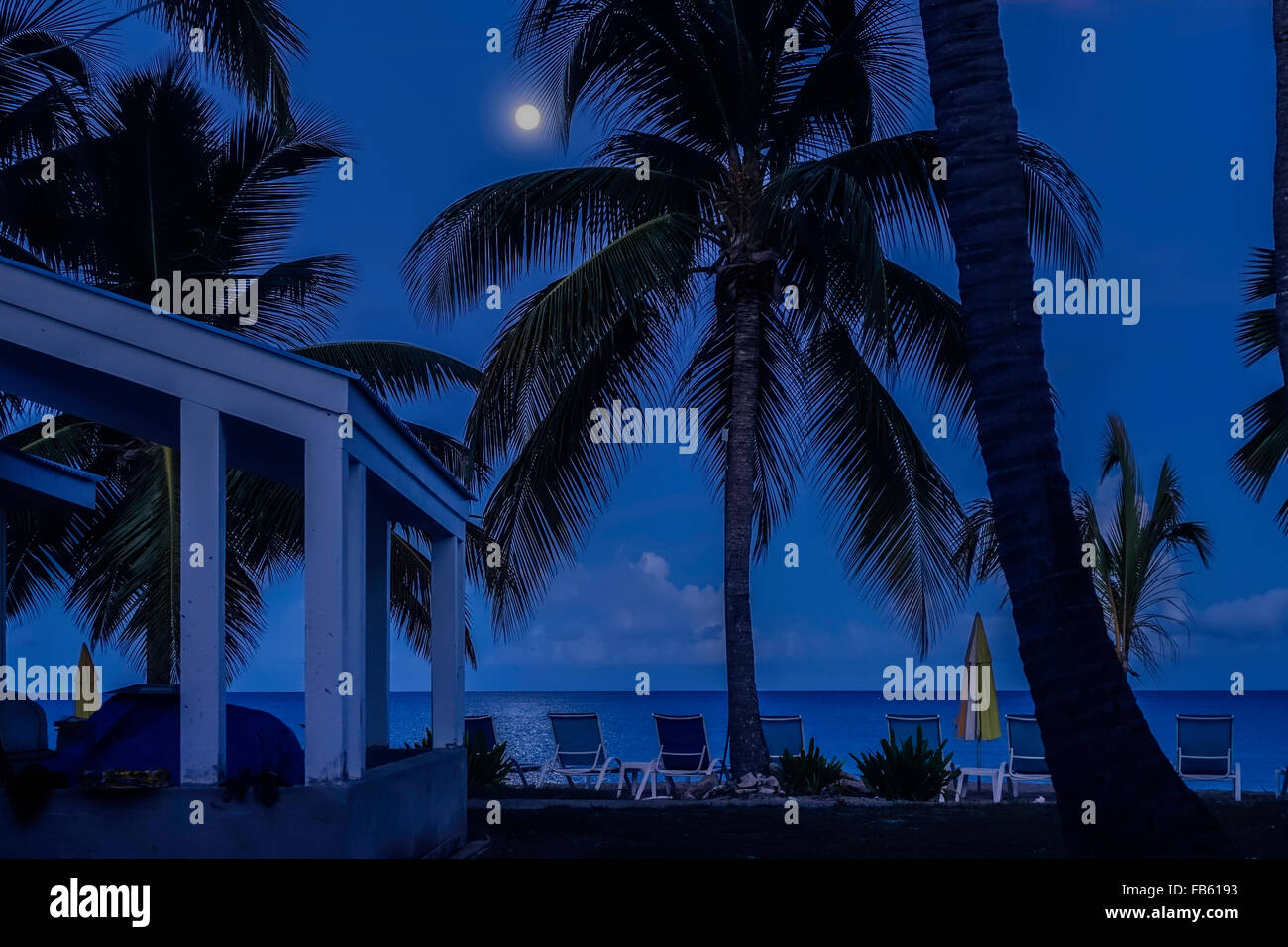 a full moon struggles through the clouds over the Caribbean sea. A palm tree beach scene. St. Croix, U.S. Virgin Islands. Cottages by the Sea resort. Stock Photo