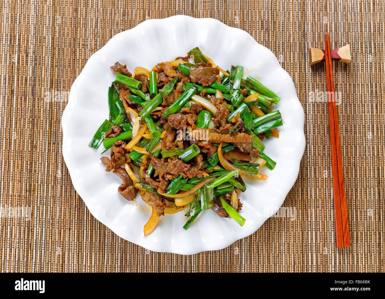 Top view of beef and green onions in white plate with bamboo mat underneath. Stock Photo