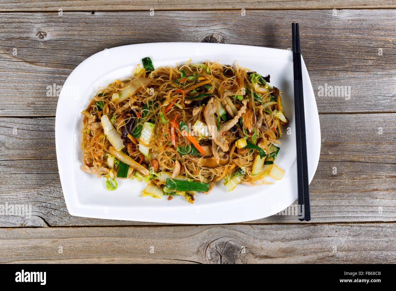 Angled view of cooked chicken strips and rice noodles with vegetables on rustic wood setting. Stock Photo