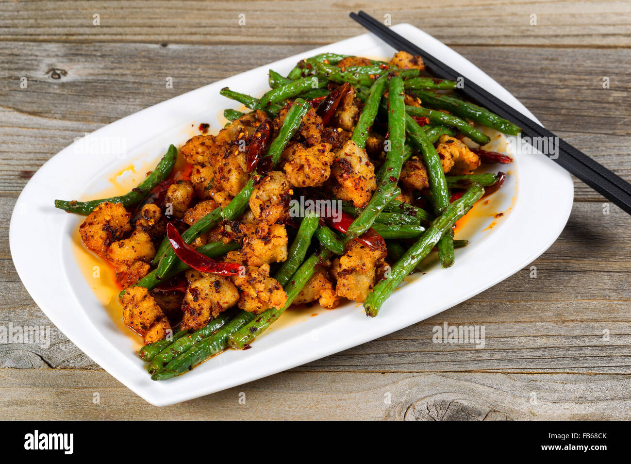 Close up view of crispy fried chicken pieces with green beans and Chile peppers on rustic wood setting. Stock Photo