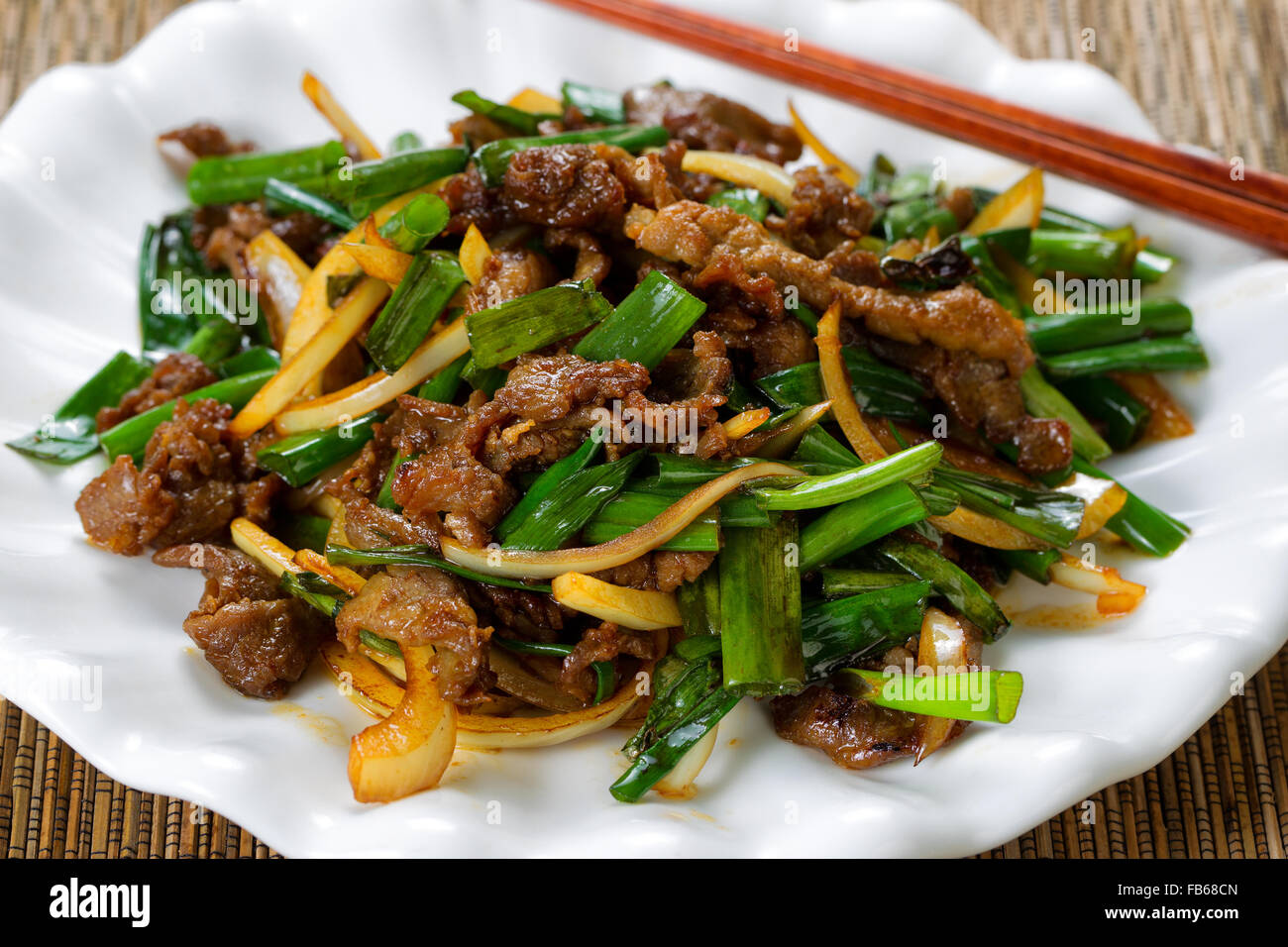 Close up view of beef and green onions in white plate with bamboo mat underneath. Stock Photo