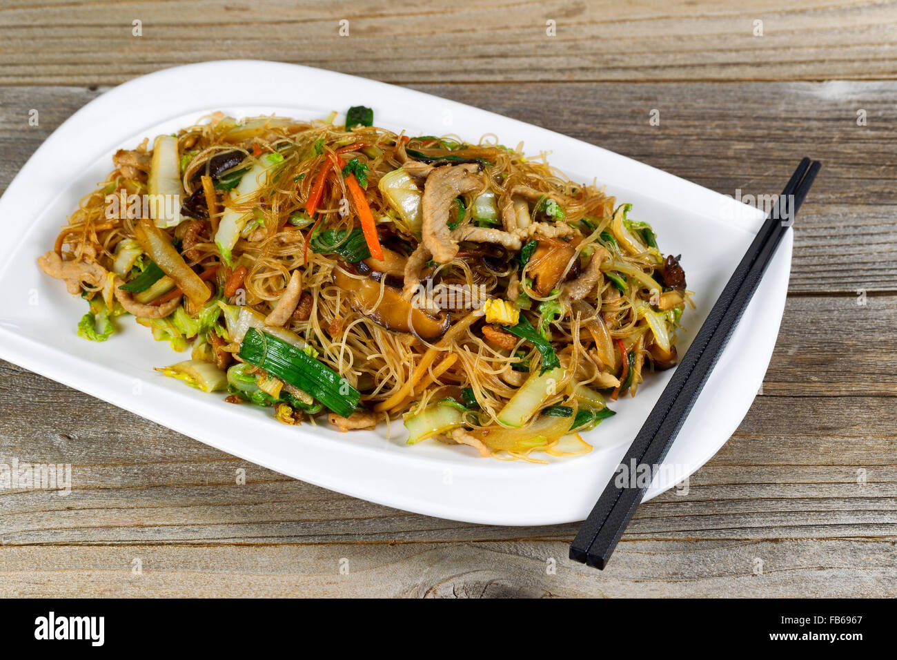 Close up view of chicken strips and rice noodles with vegetables on rustic wood setting. Stock Photo