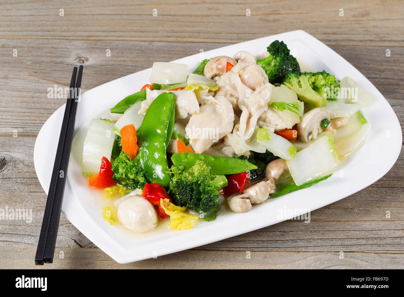 Close up view of stir fried white chicken pieces with broccoli, snow peas, peppers and mushroom in white plate. Stock Photo