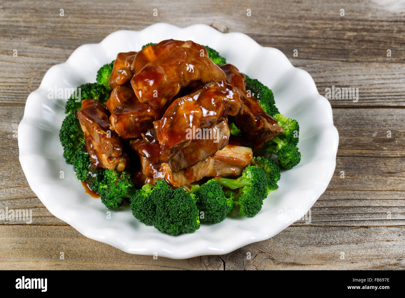 Close up view of barbecued beef ribs, in extra sauce, and broccoli in white plate on rustic wood setting. Stock Photo