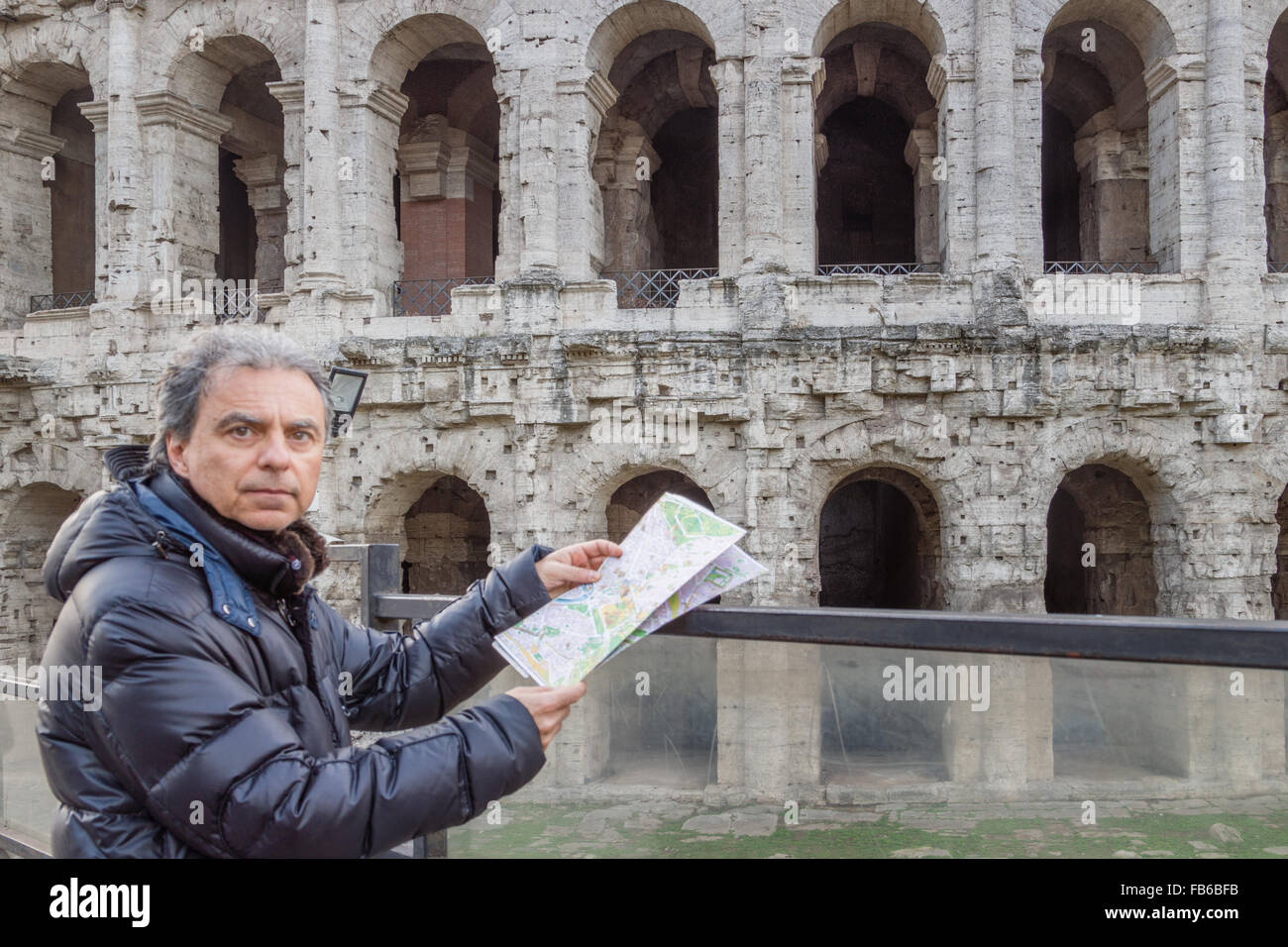 middle-aged man looks at a map near walls and arches of Roman amphitheater, the Coliseum in Rome, Italy Stock Photo