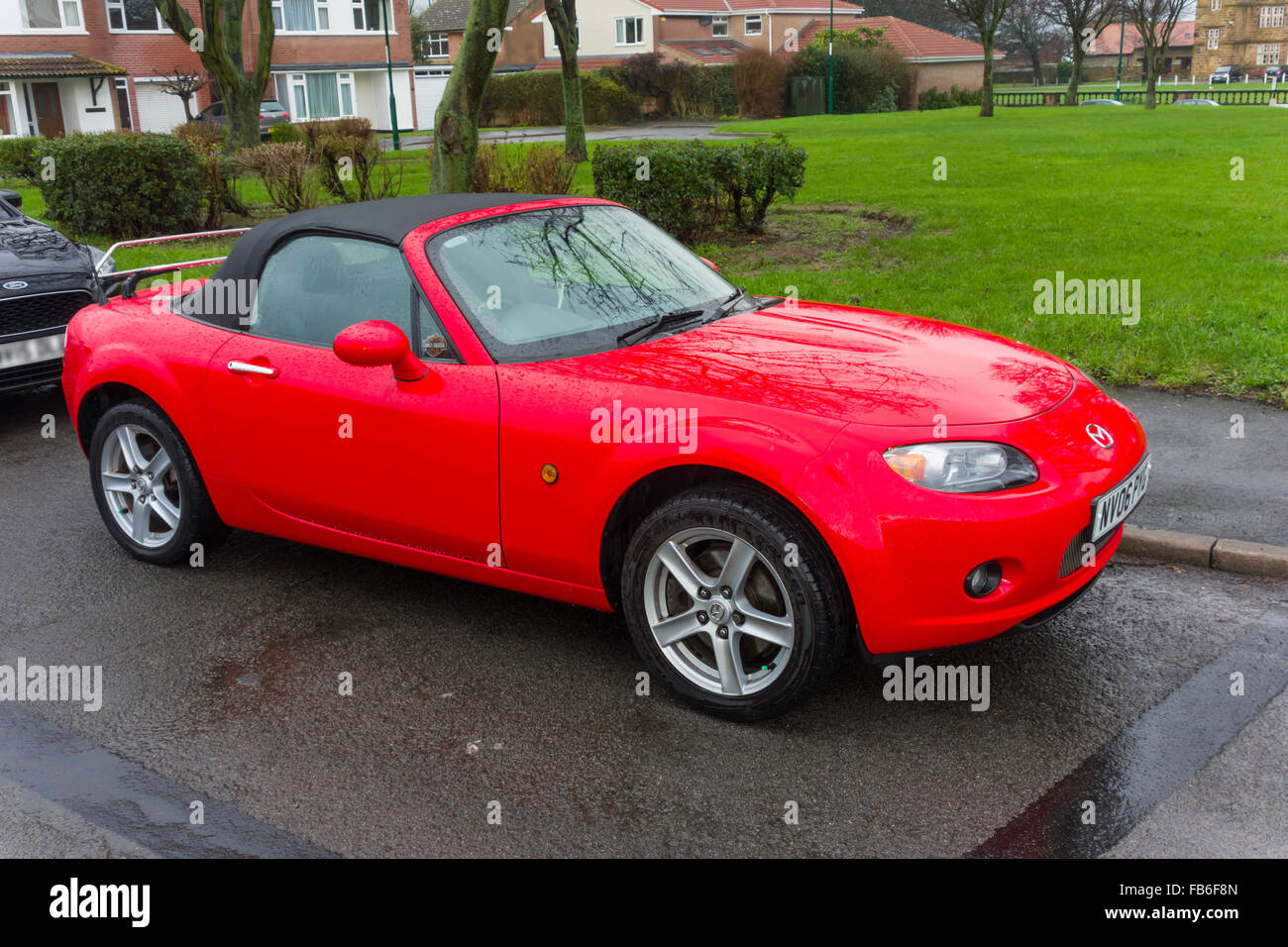 A bright red 2006 registered Mazda MX-3 soft top sports car parked in the rain Stock Photo