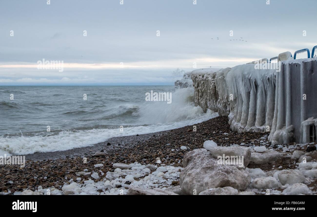 Winter Seashore Landscape. Ice covered pier with waves crashing on the beach on the coast of Lake Huron. Port Sanilac, Michigan. Stock Photo