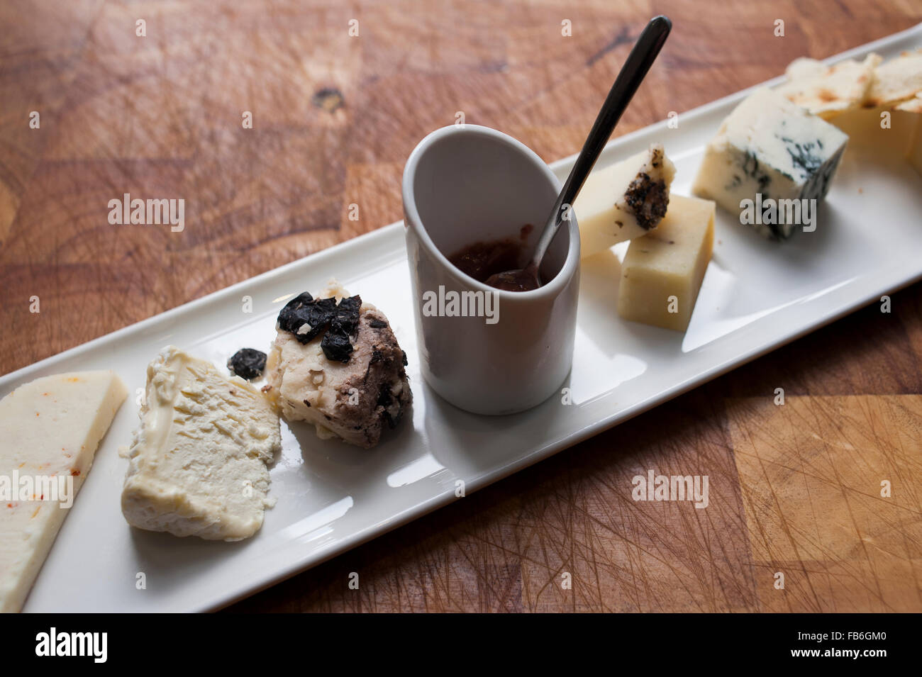 A selection of cheeses with a dish of relish presented on a white platter in an Italian restaurant. Stock Photo