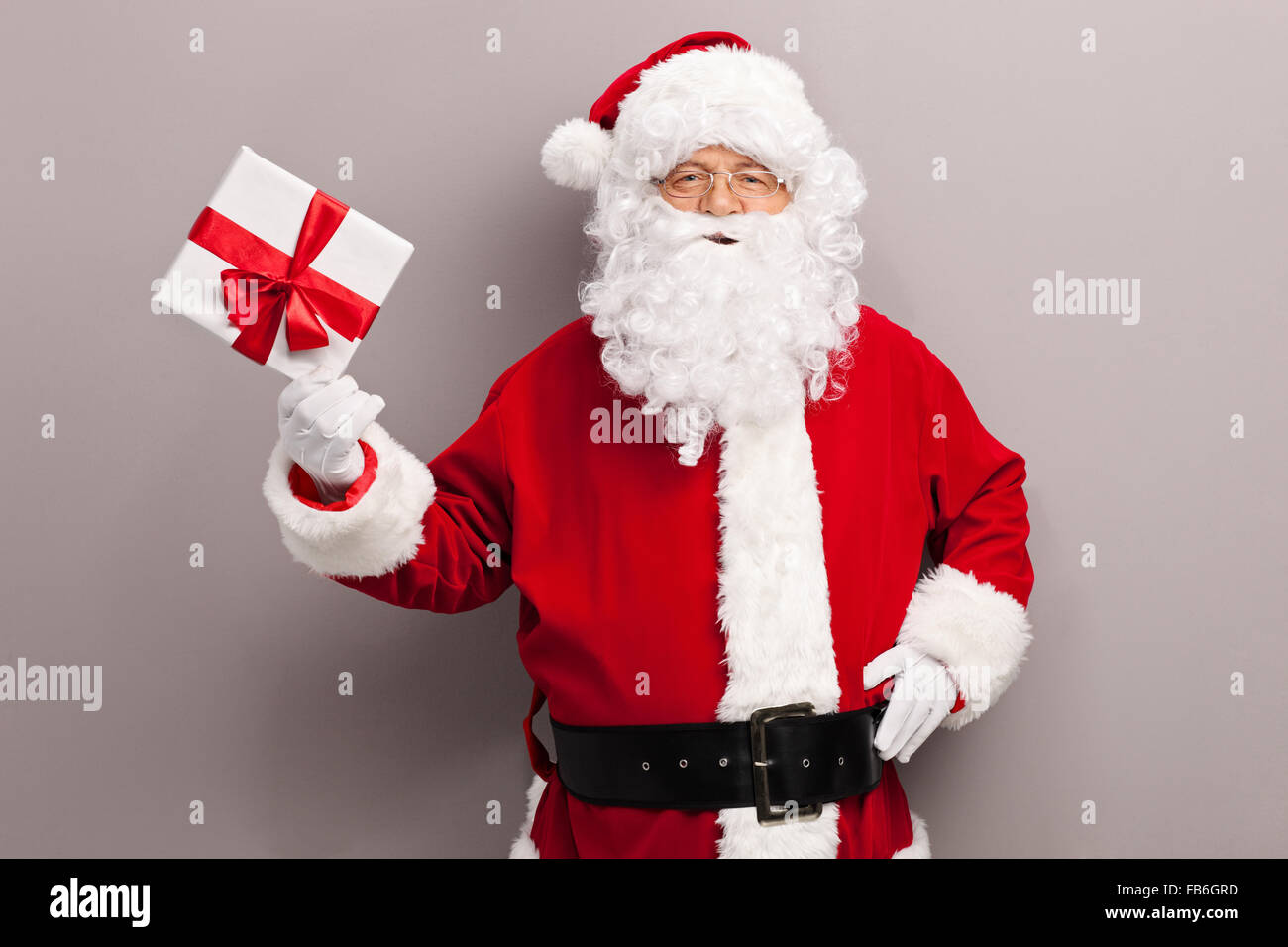 Mature man in Santa Claus costume holding a present wrapped in a white paper with a red ribbon Stock Photo