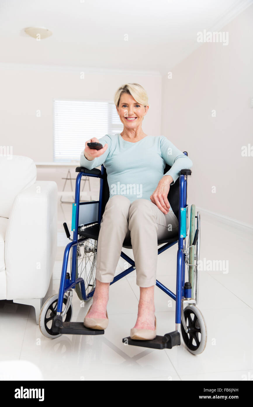 cheerful disabled senior woman watching television in living room Stock