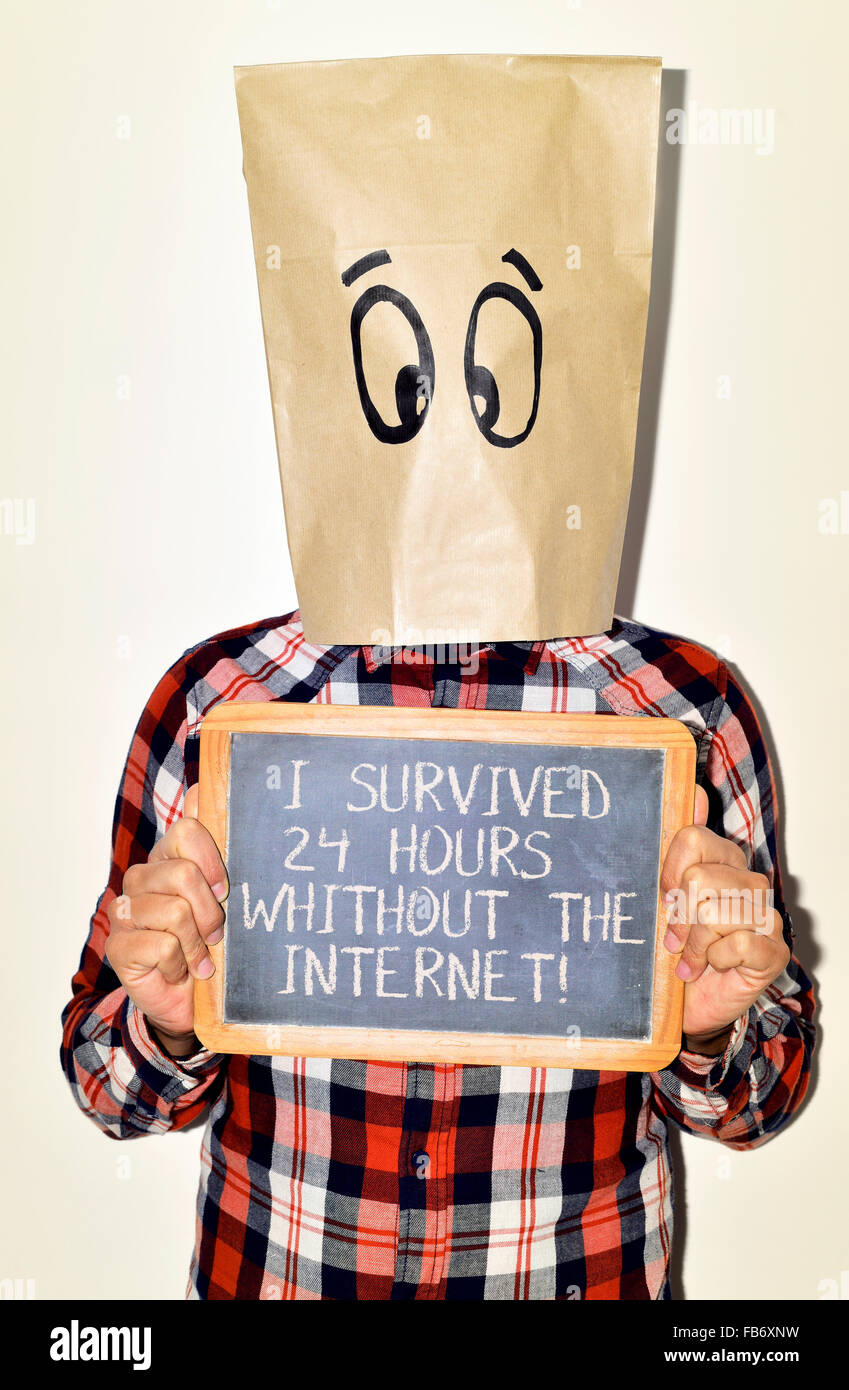 a young caucasian man with a paper bag with a funny face in his head shows a chalkboard with the text I survived 24 hours withou Stock Photo