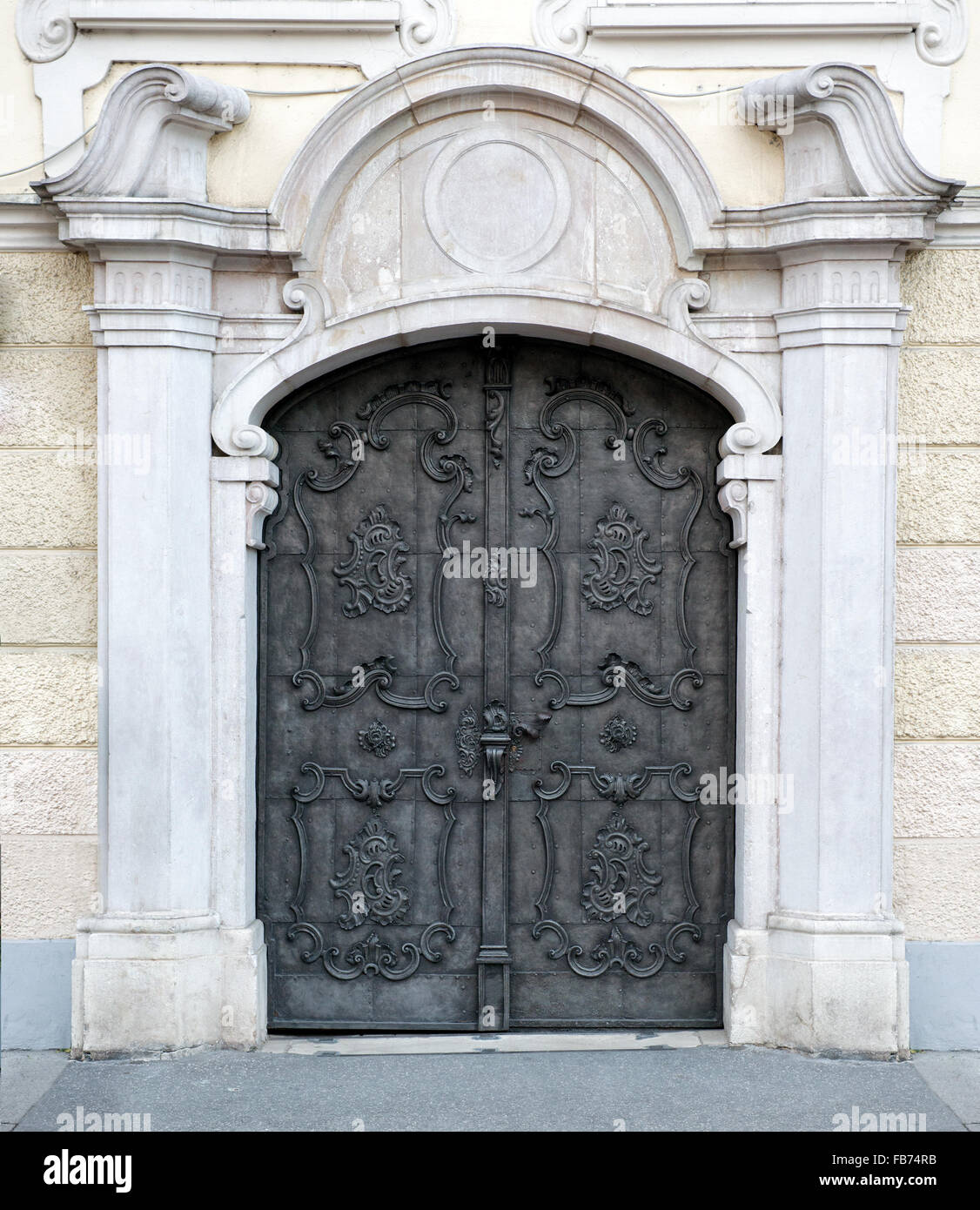 Old double carved metal Austrian door with a stone architrave and pillars opening onto a sidewalk Stock Photo