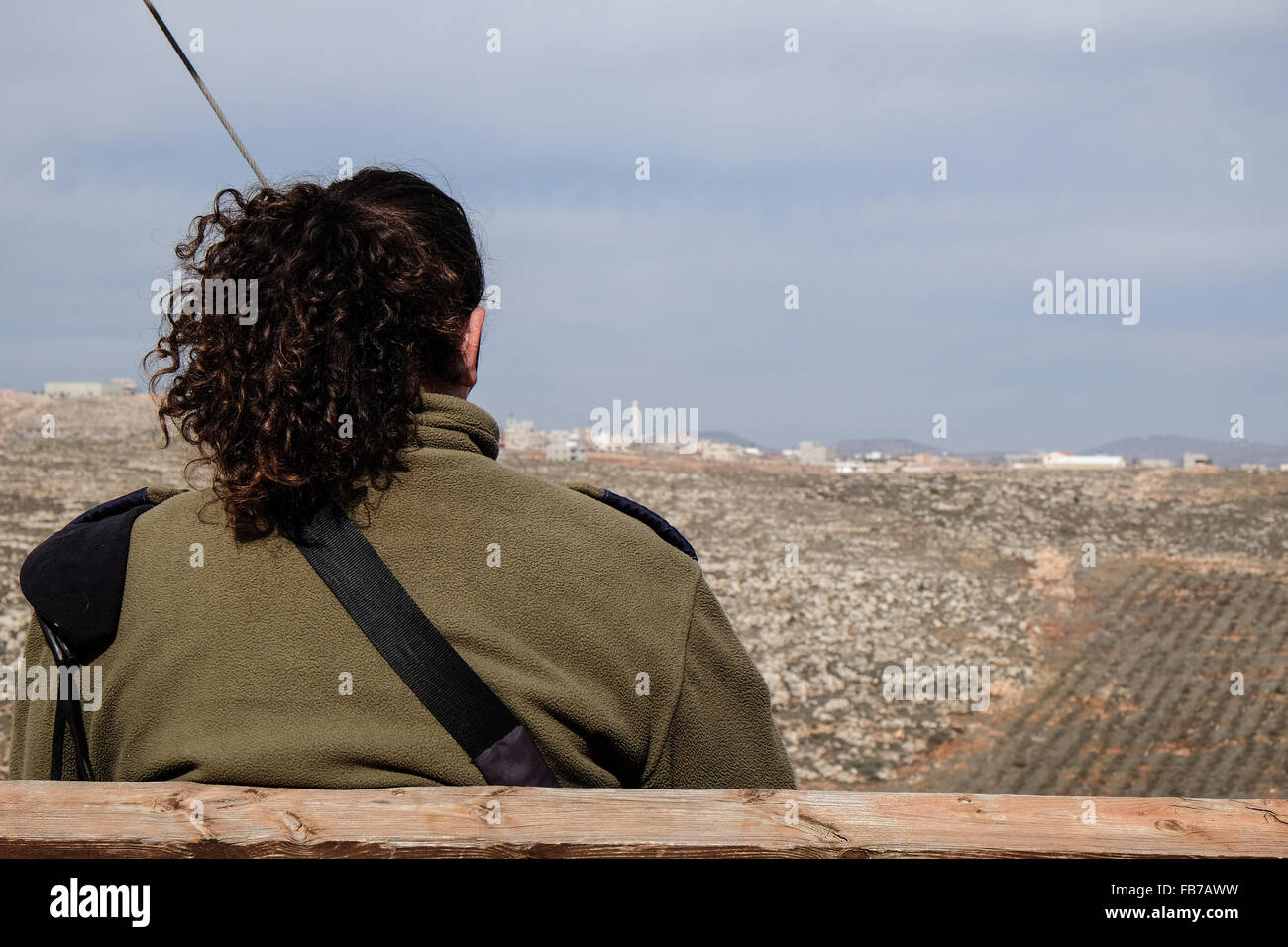 Esh Kodesh, West Bank. 11th January, 2016. An IDF officer takes a break on a bench overlooking the Palestinian village Qusra in the Esh Kodesh Israeli outpost in the West Bank near Shilo, under the jurisdiction of the Mateh Binyamin Regional Council. The settlement's guard tower is manned by IDF soldiers. The settlement was established in 1999 and is now home to some 40 families who consider it an unauthorized community of Shilo in the process of becoming formally authorized. Stock Photo