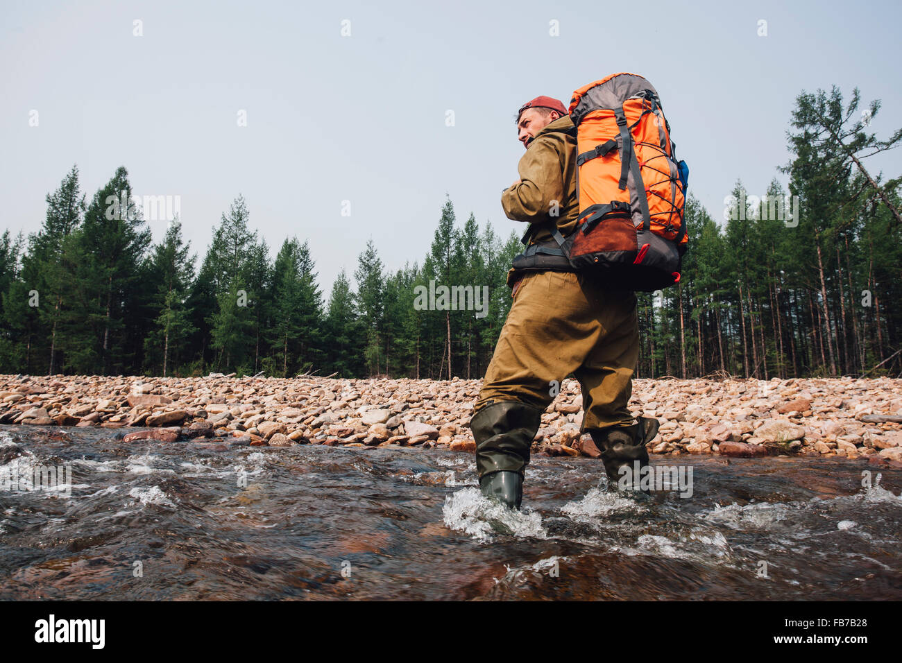 Low angle view of mid adult man with backpack standing in river at forest Stock Photo