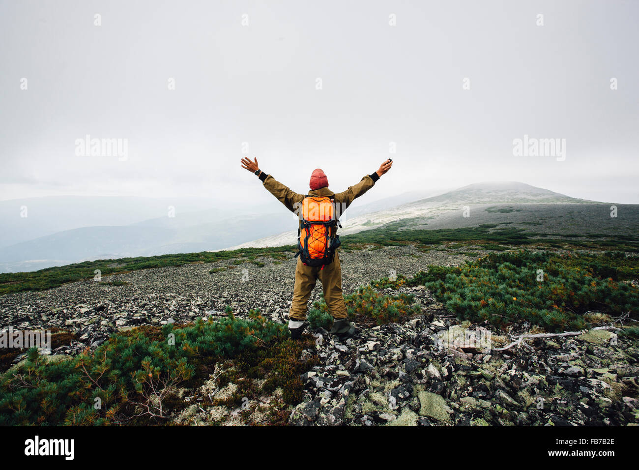 Rear view of man standing with arms outstretched on mountain Stock Photo