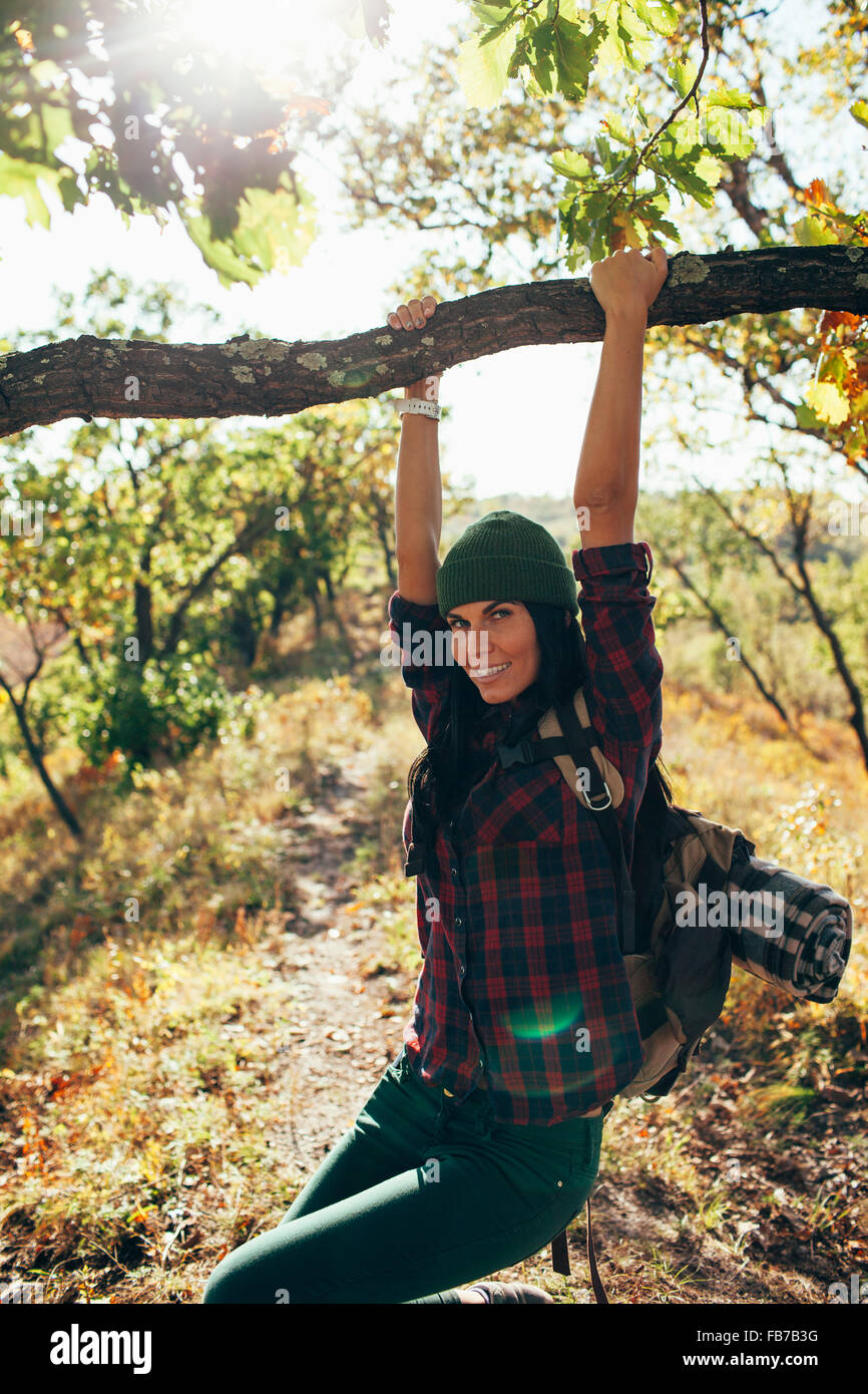 Portrait of smiling woman swinging from branch in forest Stock Photo