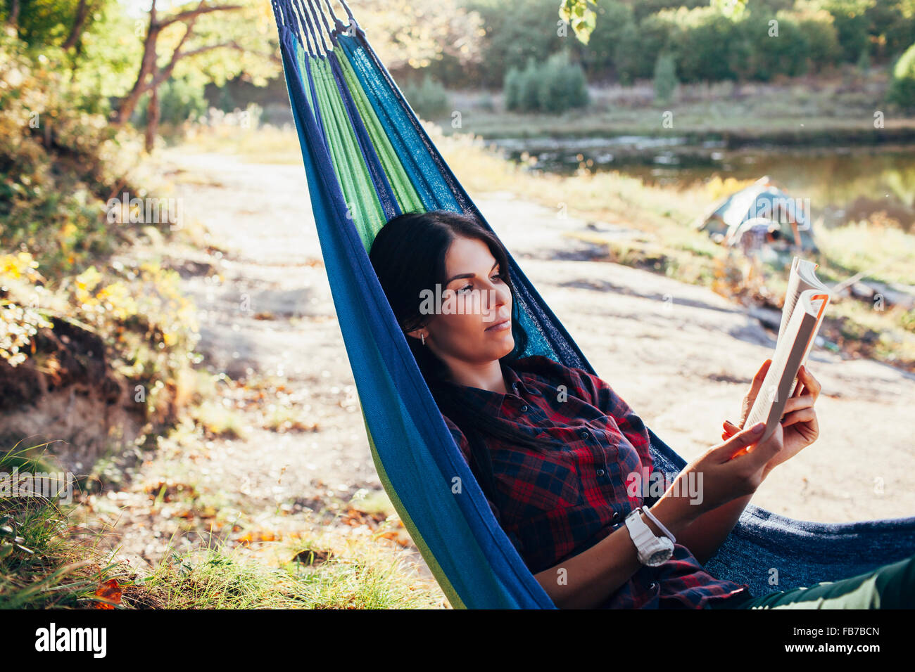 Young woman reading book while lying on hammock in forest Stock Photo