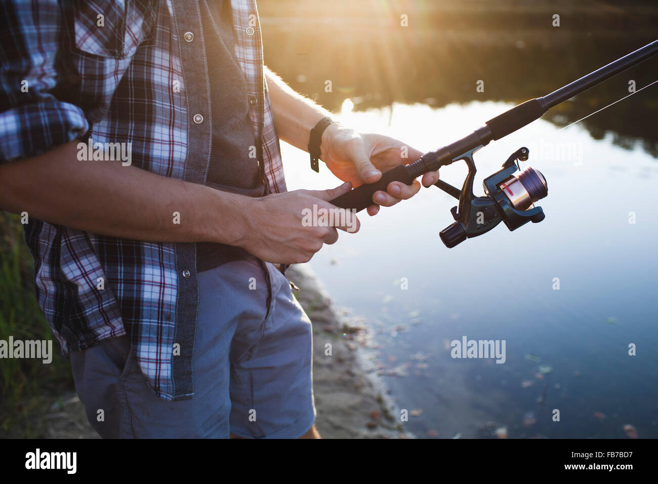 Midsection of man fishing at lakeshore in forest Stock Photo