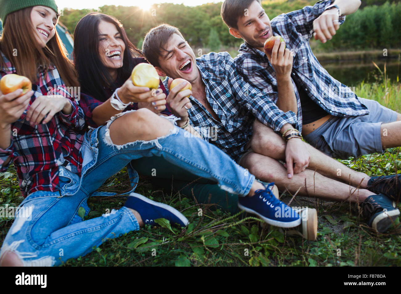 Happy friends falling on each other while having apple in forest Stock Photo