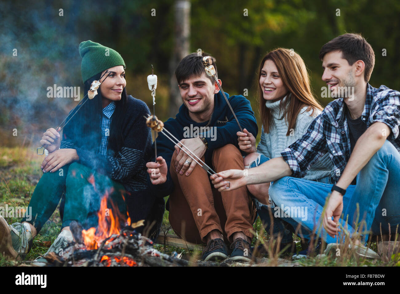 Smiling friends roasting marshmallows in forest Stock Photo