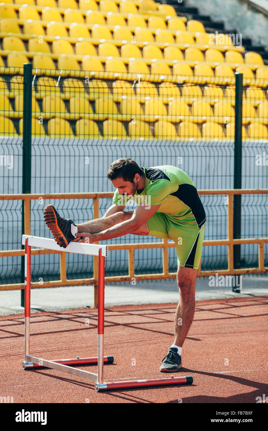Full length of track and field athlete warming up on hurdle Stock Photo
