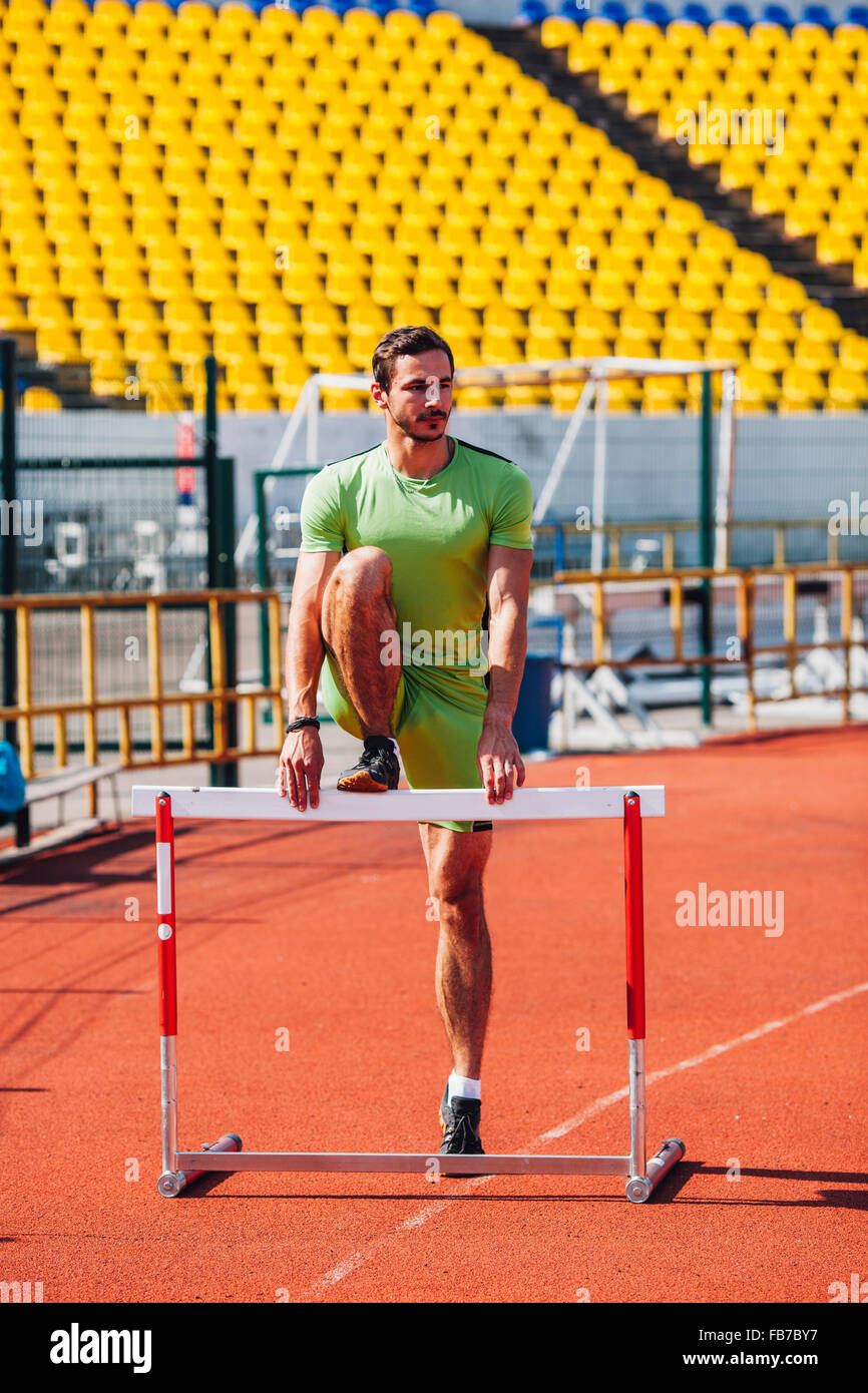 Full length of track and field athlete warming up on hurdle at sports track Stock Photo