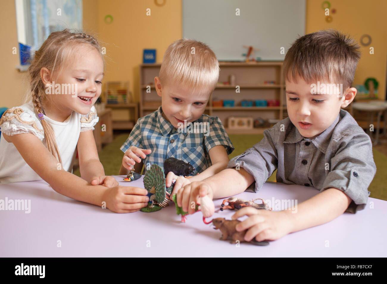 Children playing with animal toys at table in classroom Stock Photo