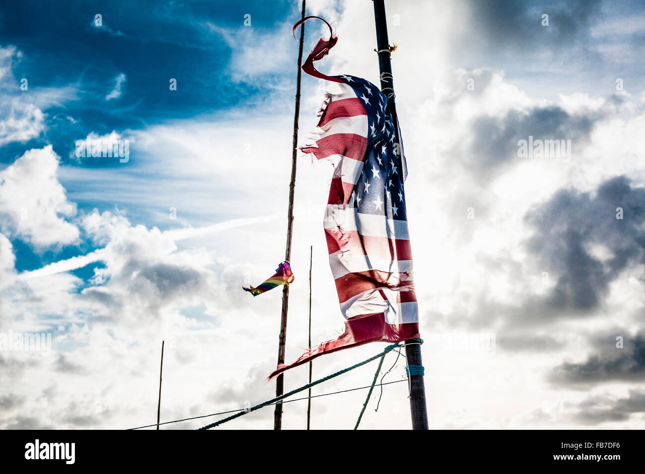 Tattered American flag on pole against cloudy sky Stock Photo