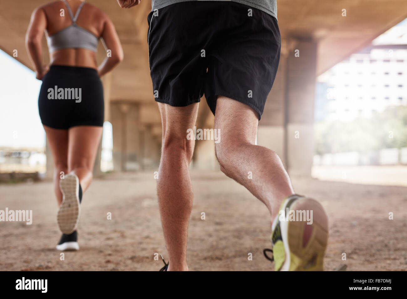 Cropped shot of a two young people running under the bridge in the city. Focus on legs of runners. Stock Photo