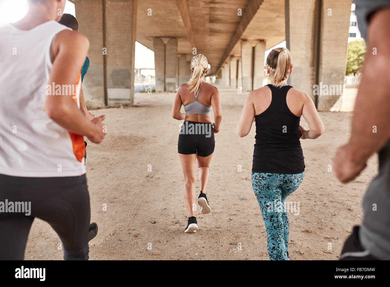 Rear view of group of athletes running under a bridge. Runners training together. Stock Photo