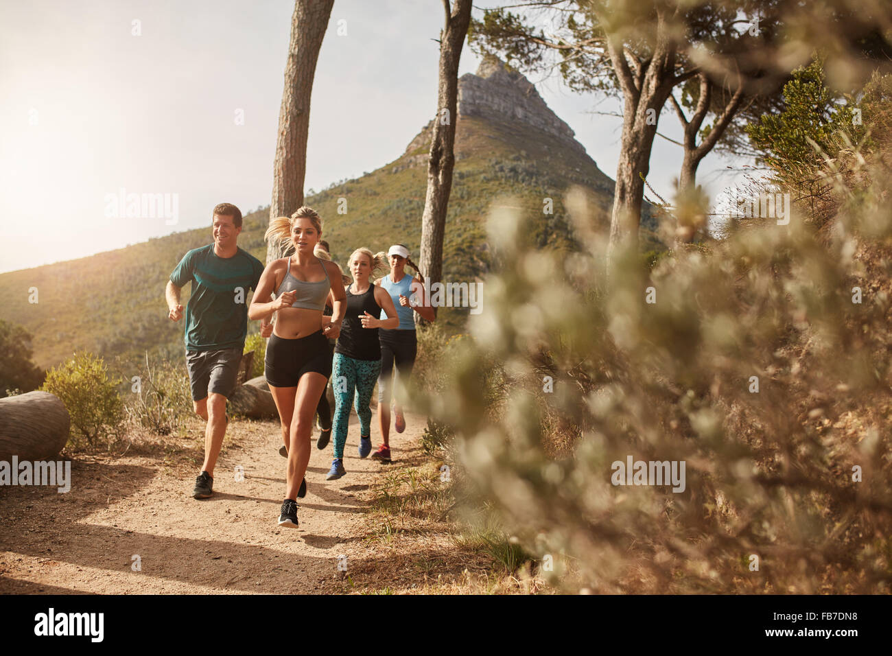 Group of young adults training and running together through trails on the hillside outdoors in nature. Fit young people trail ru Stock Photo
