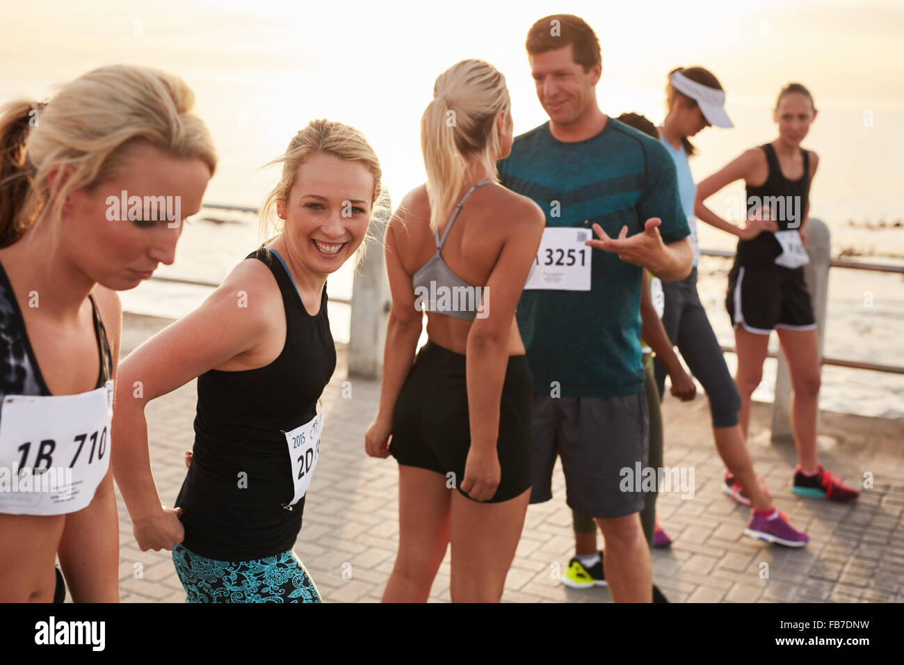 Group of happy young athletes standing on starting line and talking before start of the race. Running club group preparing for m Stock Photo