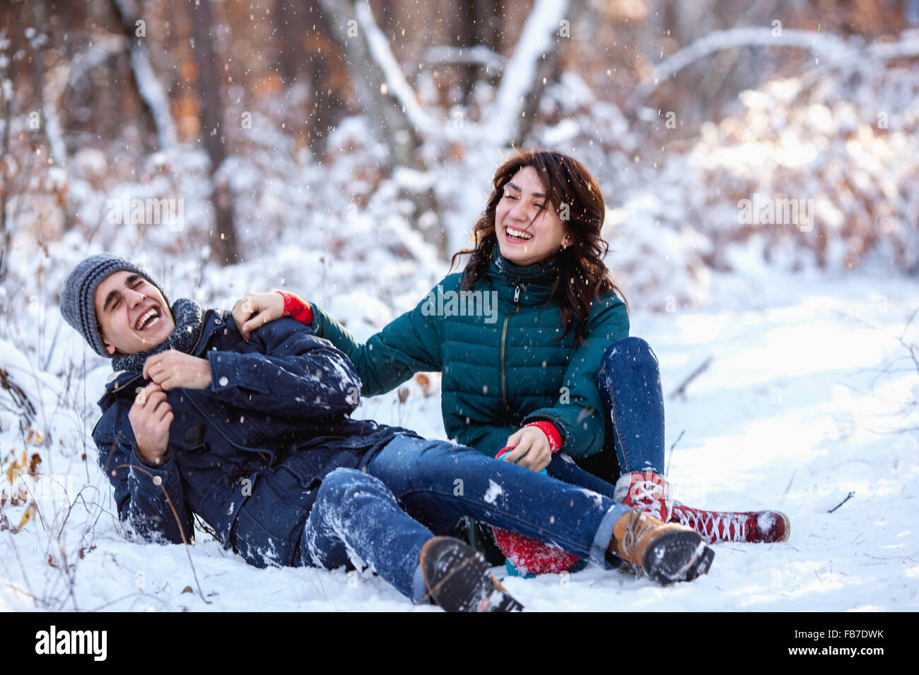Full length of playful young couple sitting on snowy field Stock Photo