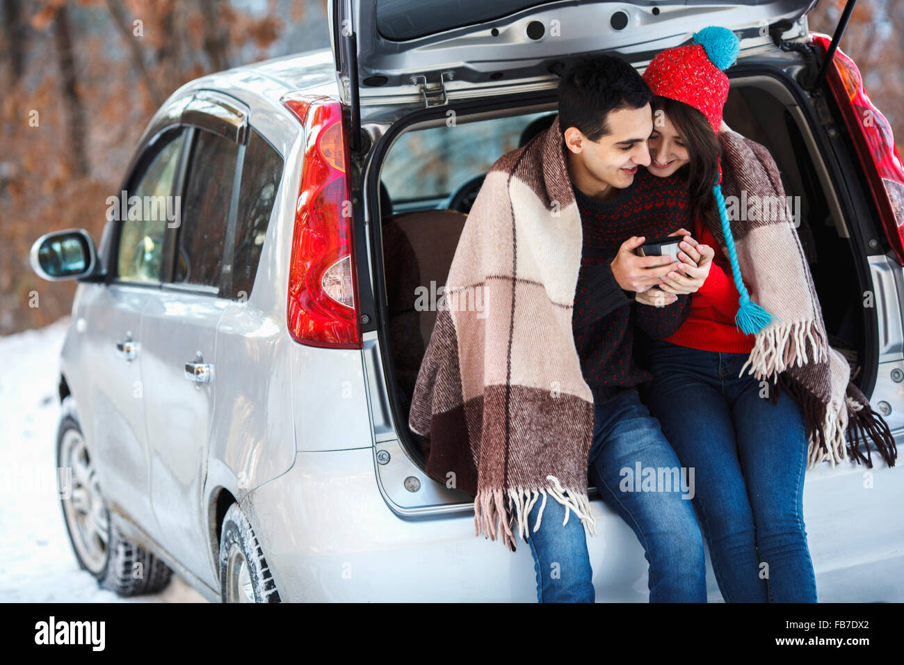 Happy young couple having coffee while sitting in boot of car during winter Stock Photo