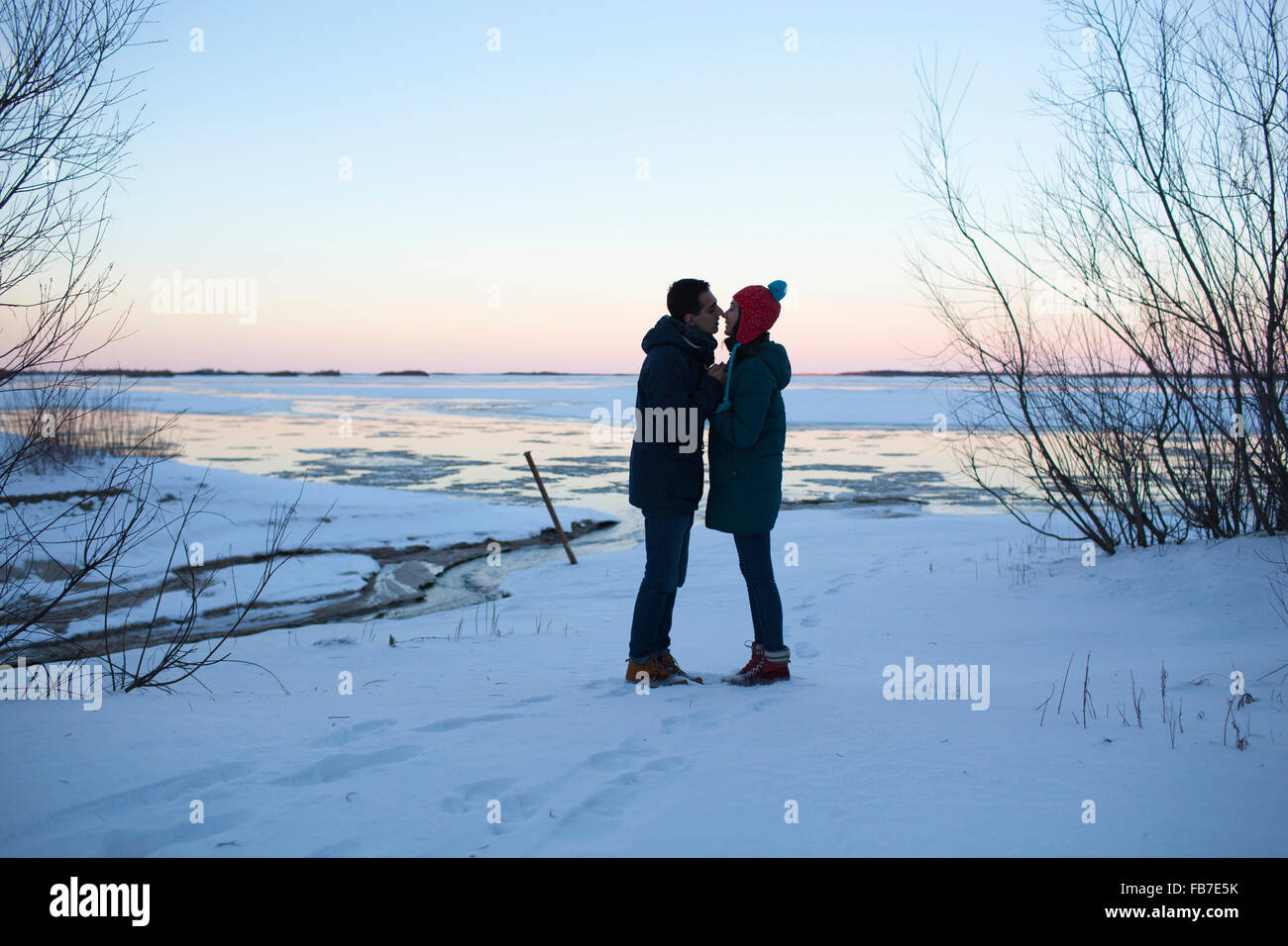 Full length side view of young couple kissing on snowy field Stock Photo