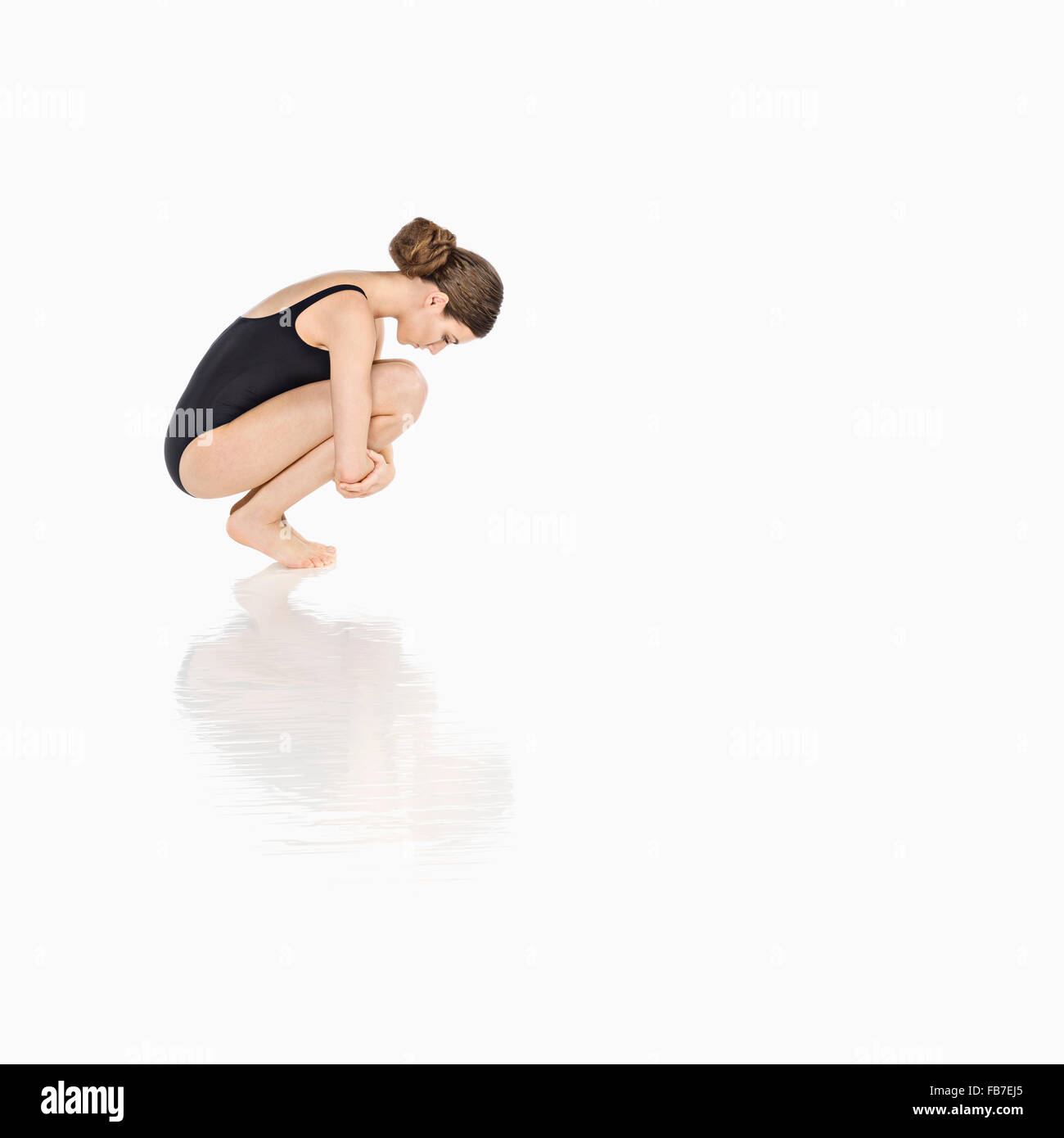 Side view of woman in bodysuit crouching over white background Stock Photo