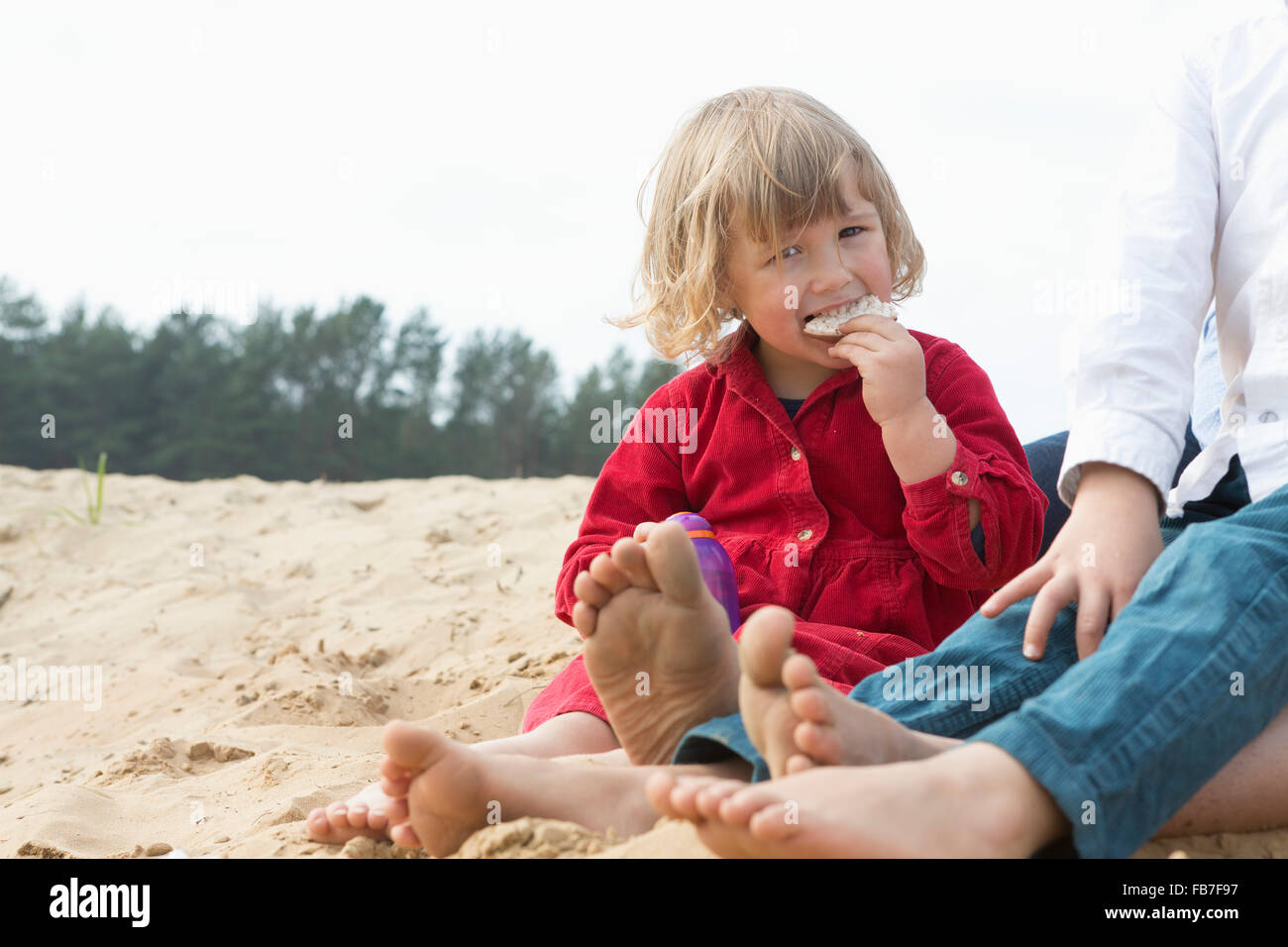 Portrait of cute girl eating snacks while sitting with family on sand Stock Photo