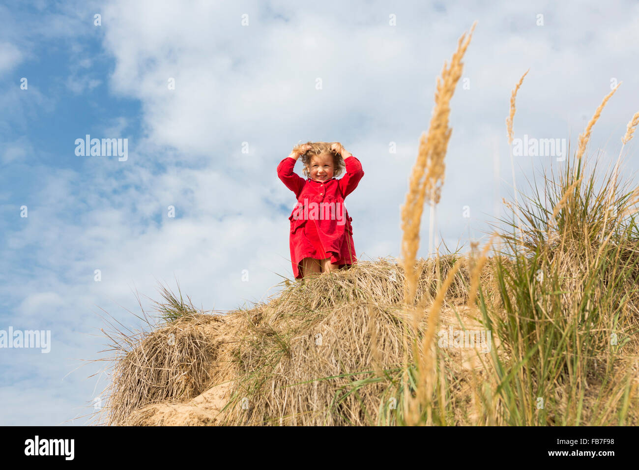 Low angle portrait of girl holding hair while standing on sand dune against sky Stock Photo