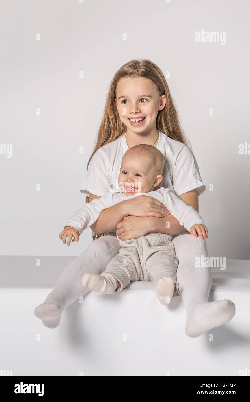 Happy baby girl sitting with sister against white background Stock Photo