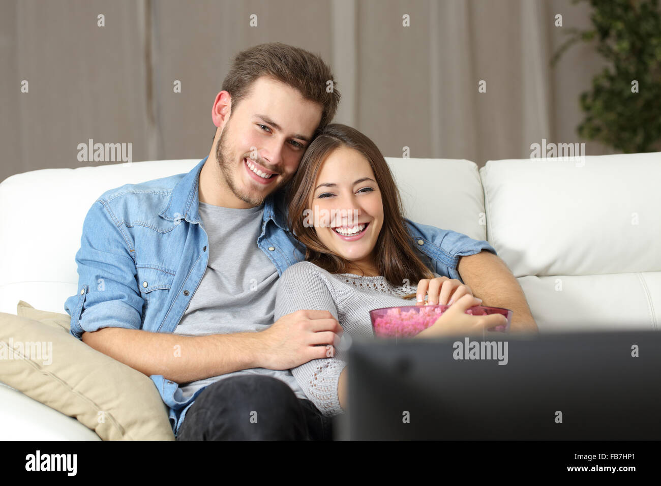 Happy couple watching a movie on tv sitting on a couch at home Stock Photo