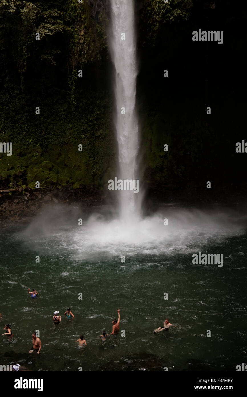 People swim in a pool at the bottom of a waterfall emerging from the