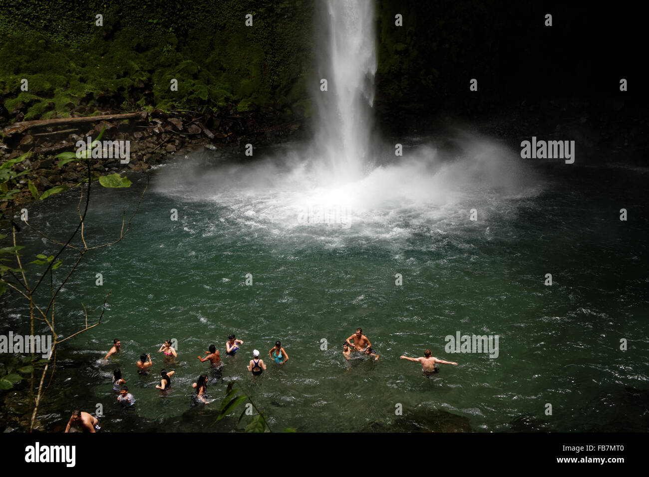 People swim in a pool at the bottom of a waterfall emerging from the
