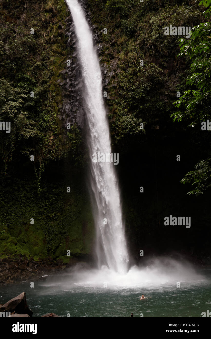 People swim in a pool at the bottom of a waterfall emerging from the