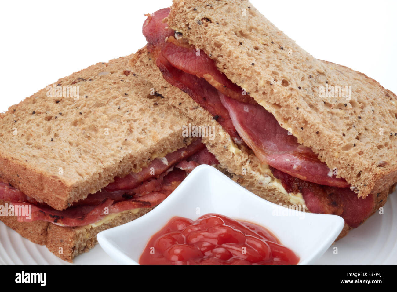 A bacon sandwich in granary brown bread with some tomato ketchup - studio shot with a white background. Stock Photo
